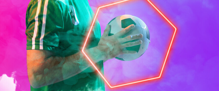 Midsection of caucasian male player holding ball by illuminated hexagon over colored background
