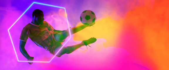 African american male soccer player jumping and kicking ball by hexagon on smoky background