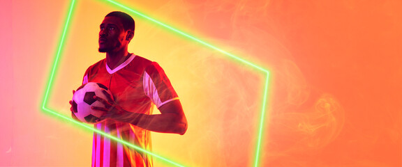 African american male soccer player holding ball by illuminated rectangle on smoky background