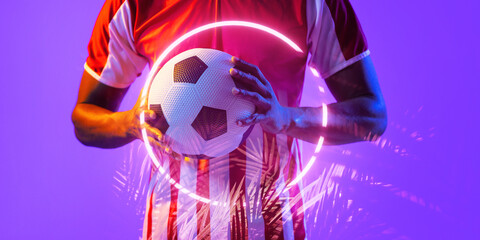 Midsection of african american male soccer player holding ball by illuminated circle and plants