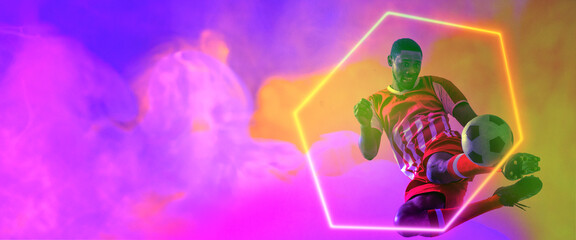 African american male player kicking soccer ball by illuminated hexagon on smoky background