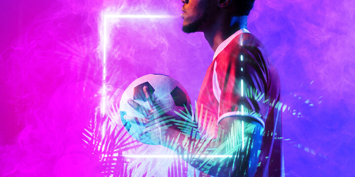Midsection of african american male soccer player holding ball by illuminated rectangle and plants