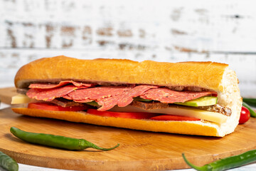 Baguette sandwich. Sandwich with salami, roast beef, cheddar, tomato and cucumber on wooden background