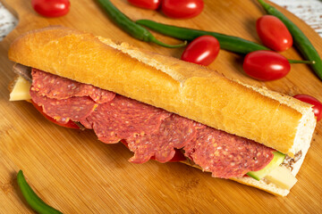 Baguette sandwich. Sandwich with salami, roast beef, cheddar, tomato and cucumber on wooden background