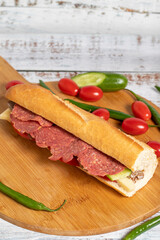Baguette sandwich. Sandwich with salami, roast beef, cheddar, tomato and cucumber on wooden background