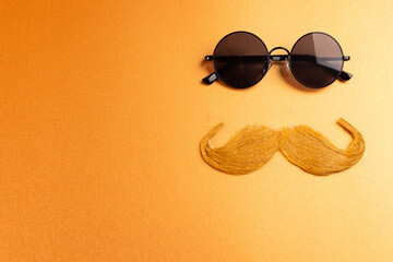 Composition of fake moustache and glasses on orange background with copy space