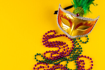 Composition of colourful mardi gras beads and carnival mask on yellow background with copy space