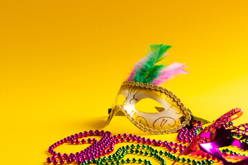 Composition of colourful mardi gras beads and carnival masks on yellow background with copy space © vectorfusionart