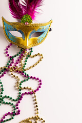 Composition of colourful mardi gras beads and carnival mask on white background with copy space