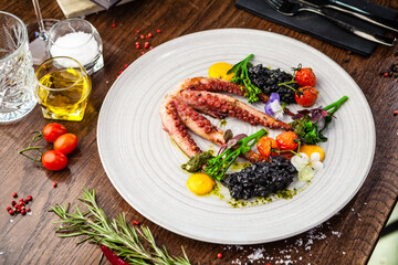 Octopus with black risotto. Carrot cream, mini-broccoli, basil pesto. Delicious healthy traditional food closeup served for lunch in modern gourmet cuisine restaurant