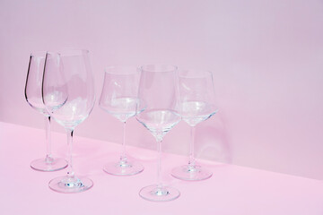 Various empty wine glasses on a pink background with space for text.