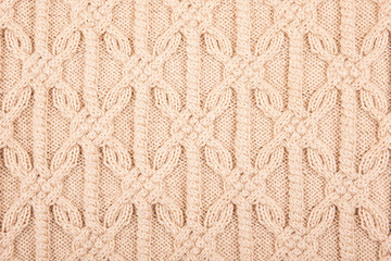 Knitted beige background. Large knitted fabric with a pattern. Close-up of a knitted blanket. Horizontal ornament.