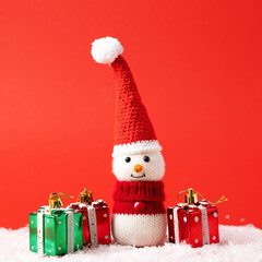 Knitted snowman in a red Christmas hat and sweater with green and red gifts. Merry Christmas and New Year 2023 greeting card