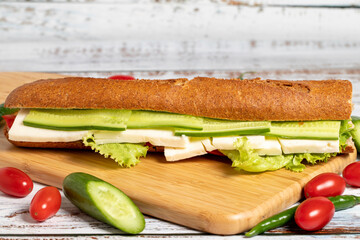 Baguette sandwich. Sandwich with olives, lettuce, tomato, cucumber, cheddar and feta cheese on wooden background