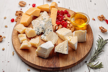 Pieces of various cheeses with nuts and honey, on a white wooden background