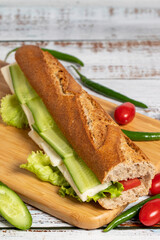 Baguette sandwich. Sandwich with olives, lettuce, tomato, cucumber, cheddar and feta cheese on wooden background