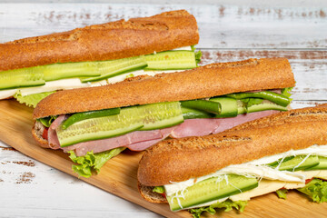 Variety of delicious baguette bread sandwiches on cutting board. Salami, smoked meat, olives, lettuce, tomato and cucumber sandwich