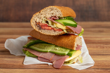 Baguette sandwich. Sandwich with salami, smoked meat, olives, lettuce, tomato and cucumber on wooden background