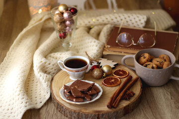 Cup of tea or coffee, various sweets and spices, Christmas decorations, comfy blanket, books and glasses. Selective focus.