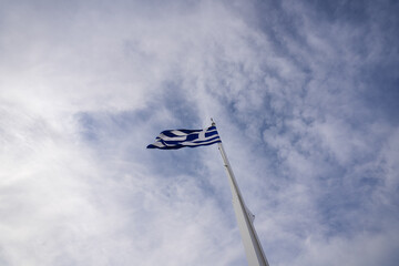 Wide angle view from the bottom of the pole to the top with the Greece flag winding against cloudy sky.