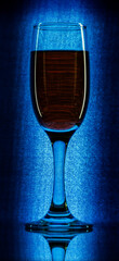 One glass of champagne in the background lighting on a black table. Silhouette of a champagne glass on a black background in a color reflection