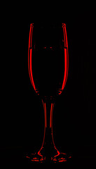 One glass of champagne in the background lighting on a black table. Silhouette of a champagne glass on a black background in a color reflection