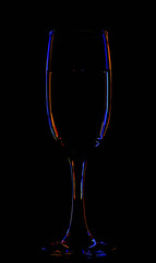 One glass of champagne in the background lighting on a black table. Silhouette of a champagne glass on a black background in a colored background.