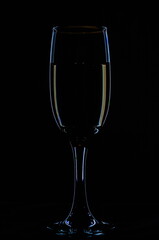 One glass of champagne in the background lighting on a black table. Silhouette of a champagne glass on a black background in a colored background.