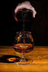 bartender pours the cognac or brandy in big glass on the old bar counter