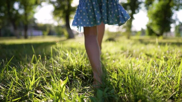 Little cheerful girl with bare feet run along green grass in nature.Foot of child is large on grass in rays of sun.Active childhood outdoors.Healthy lifestyle.Girl child play and run in park in summer