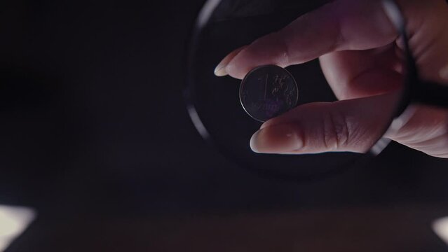 examination of a 2 euro coin under a magnifying glass on a black background, coin authenticity check, close-up, static shot