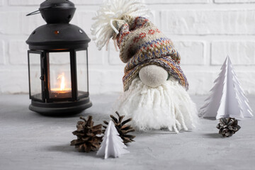 Fototapeta premium A small gnome in a cap with a bubo, beard and a big nose with a flashlight, Christmas tree candles and cones. Decor for christmas in scandinavian style