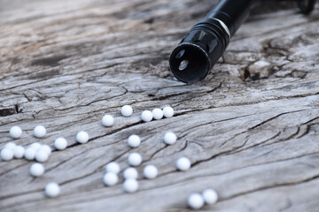 BB gun or airsoft gun muzzle and white bullets on wooden plank, soft and selective focus.