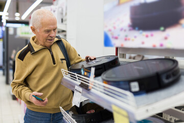 elderly man choosing robot vacuum cleaner in showroom of electrical appliance store