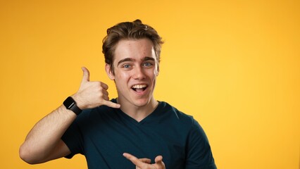 Portrait of smiling happy young man 20s smiling and giving call me gesture with hands isolated on...