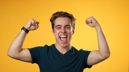 Excited jubilant overjoyed young man 20s doing winner gesture celebrate clenching fists say yes...