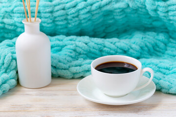Cup of coffee, aroma reed diffuser and a turquoise knitted blanket