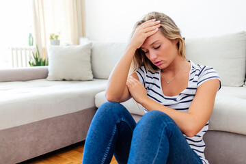 Obraz premium Anxious worried woman sitting on couch at home. Frustrated confused female feels unhappy, problems in personal life, quarrel breakup with boyfriend and unexpected pregnancy concept.