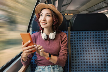 A girl surfing the internet in her mobile phone while traveling on a train with headphones
