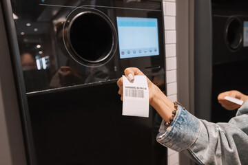 A student girl hands over a plastic beverage bottle for recycling to automated machine and having a...