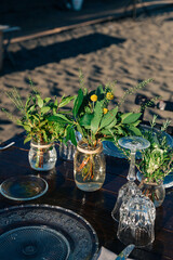 Particolare di decorazione floreale per feste. Vasetti di vetro contenenti erbe aromatiche e fiori, sulla tavola in riva al mare