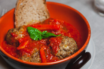 polpette di carne su sugo di pomodoro rosso con foglia di basilico e fetta di pane tostato in ciotola di terracotta