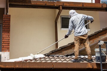 Worker adding undercoat foundation paint onto rooftop with roller at residential building in...