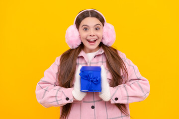 shocked child in earmuffs and mittens hold present box on yellow background, giftbox