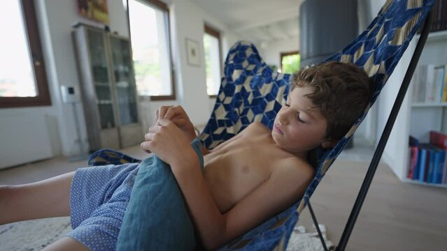 One bored young boy sitting at living room home with nothing to do. Authentic upset preteen kid feeling dullness. Real life sad child in boredom