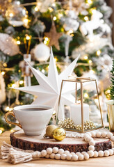 Lifestyle. A cup of tea, a Christmas tree, candles and golden balls on a wooden table against a beautiful bokeh background during the Christmas holidays. Still-life. The concept of home warmth,comfort