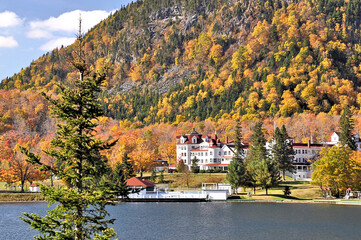 Fototapeta na wymiar Treelined mountainside of colorful fall foliage above Lake Gloriette and historic Balsams Grand Resort Hotel in remote Dixville Notch, New Hampshire.