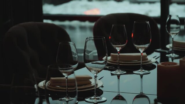Glass glasses and white plates. Close-up table setting in the dark interior of the restaurant. The decor of the festive table. The plate is on a black glass table, slow motion shot.