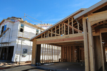 Framed garage and adjacent house under construction highlight early stages of residential building, showing exposed wooden beams, trusses, and sheathing installation