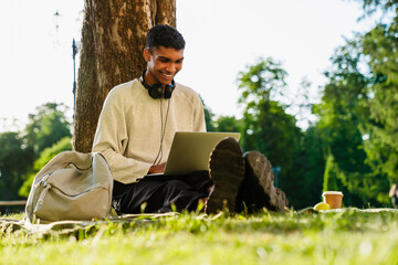 Young african man working on laptop while sitting outdoors in park